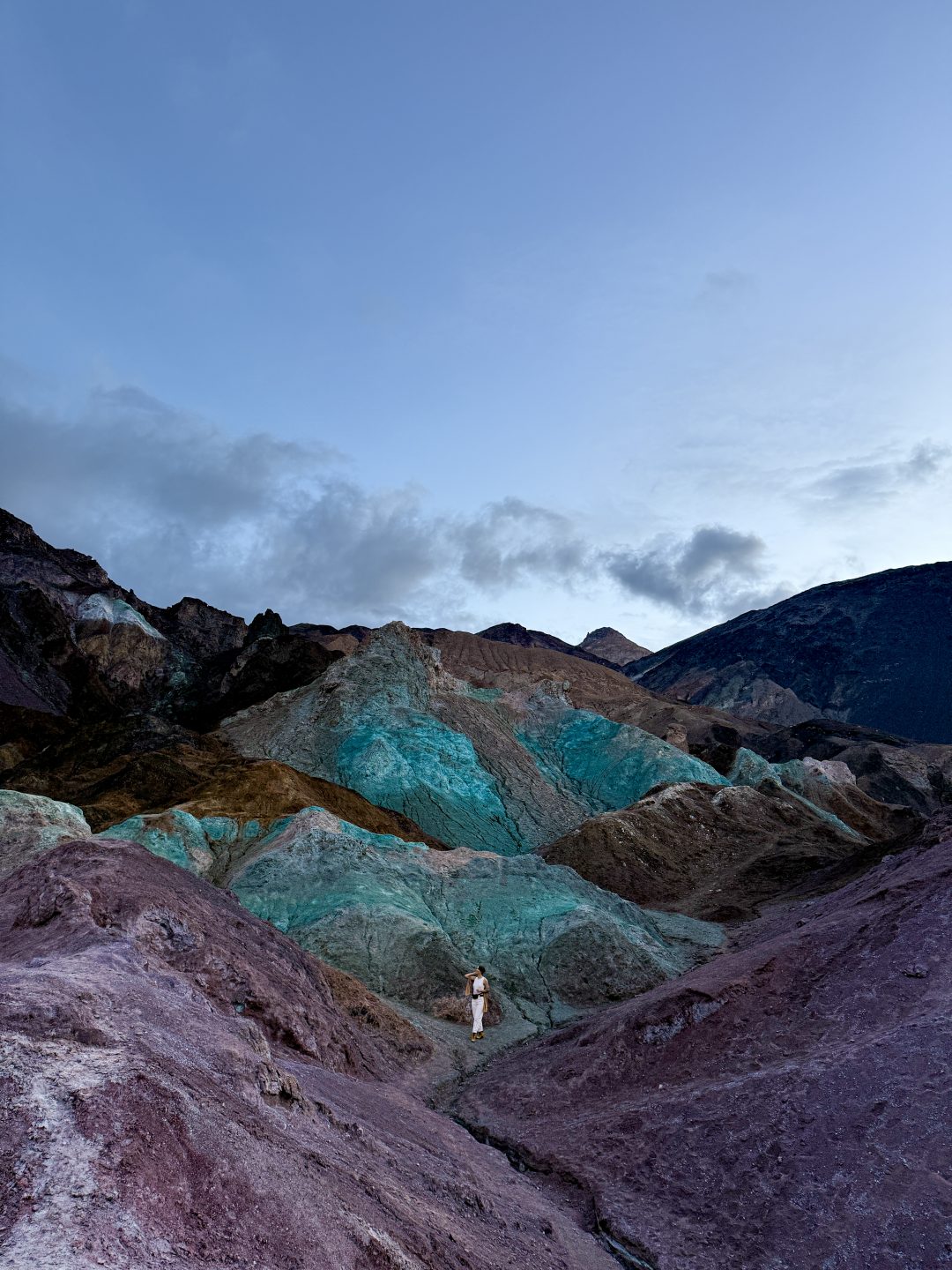 An edited photo of Travel Blogger Jordan Gassner standing in between two purple hills and in front of a blue hill at Artist's Palette in Death Valley, California
