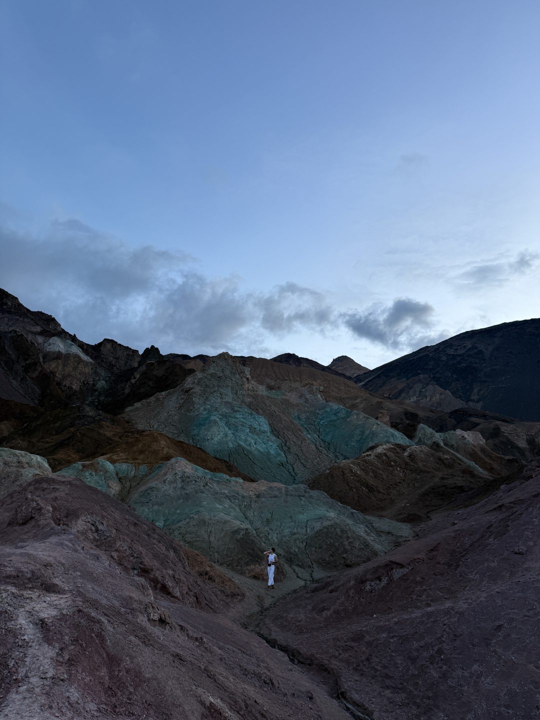 An unedited photo of Travel Blogger Jordan Gassner standing in between two purple hills and in front of a blue hill at Artist's Palette in Death Valley, California