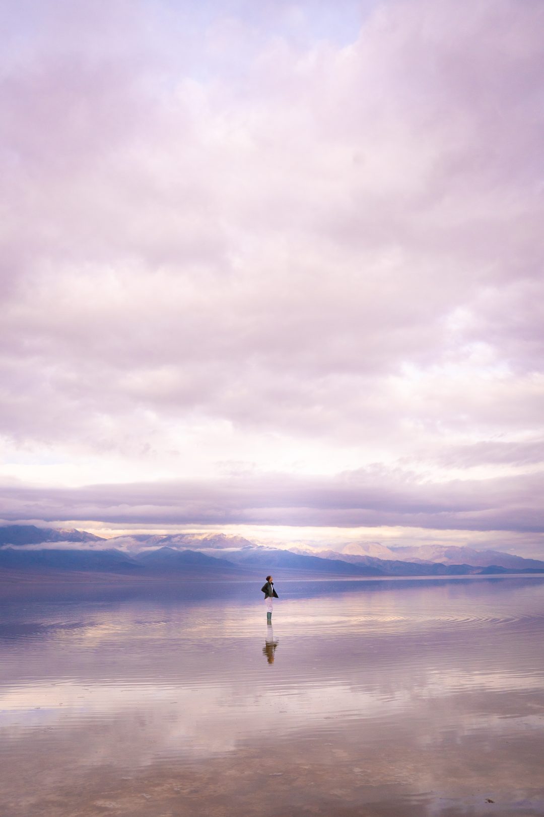 Travel Blogger Jordan Gassner adjusting her sweatshirt while standing on a flooded plateau known as Badwater Basin in Death Valley National Park in California