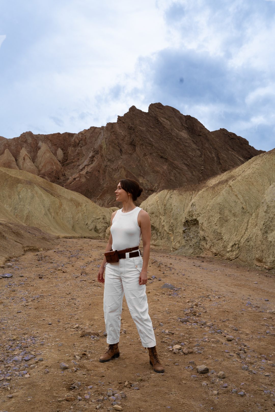 Travel Blogger Jordan Gassner standing along a path in between two yellow hills with a red mountain behind inside Golden Canyon in Death Valley National Park