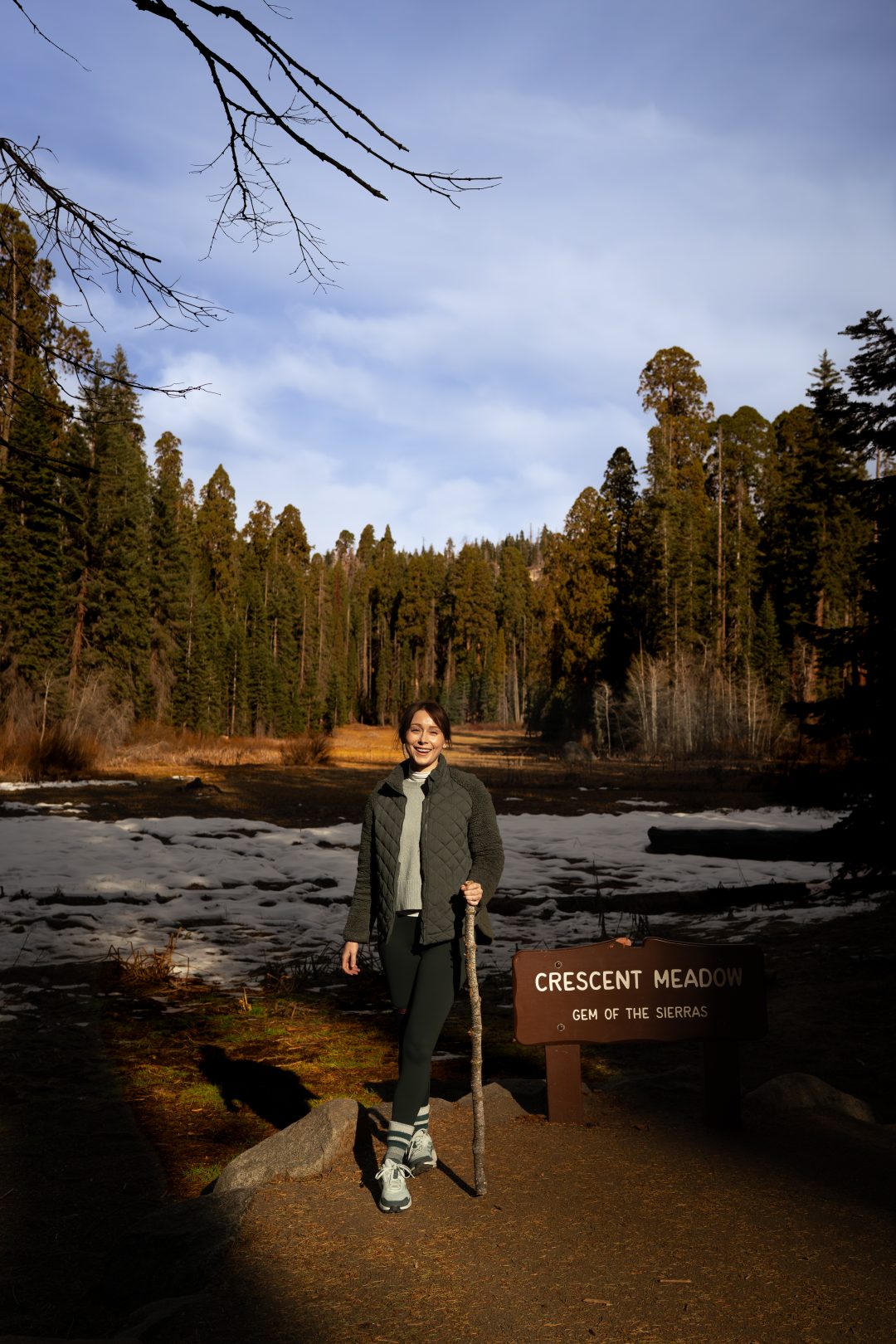 Travel Blogger Jordan Gassner smiling and holding a walking stick in front of Crescent Meadow during a Sequoia National Park Trip