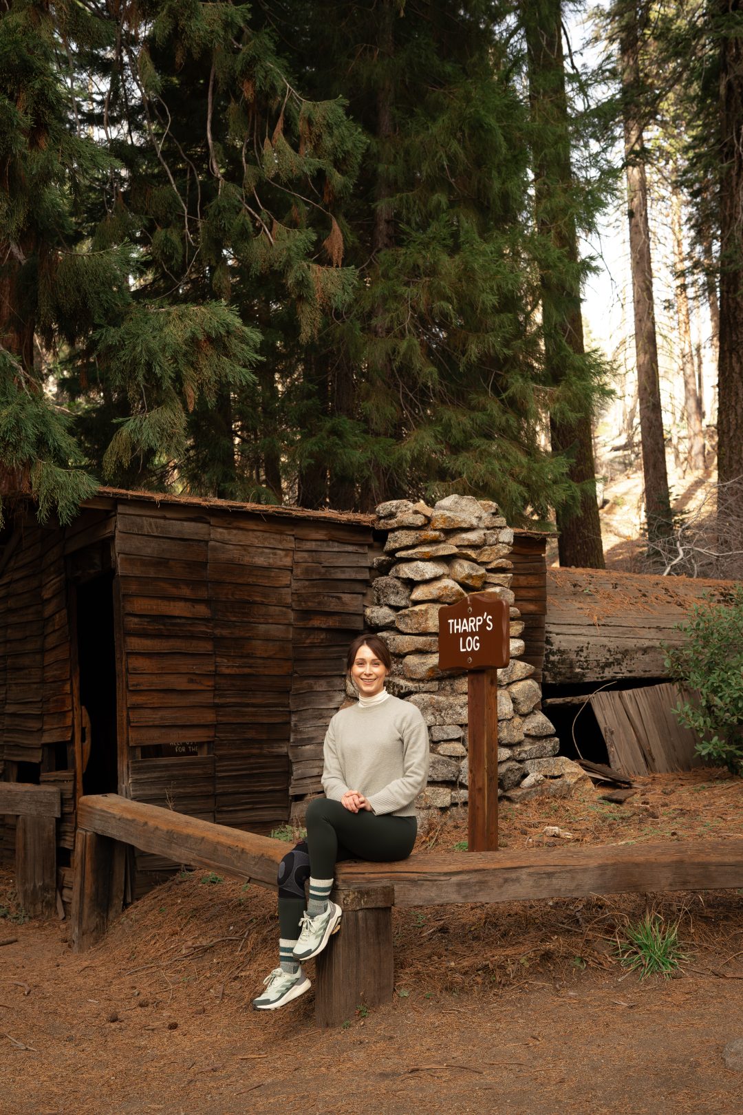 Travel Blogger Jordan Gassner smiling while sitting on a bench in front of Tharp's Log in Sequoia National Park Trip