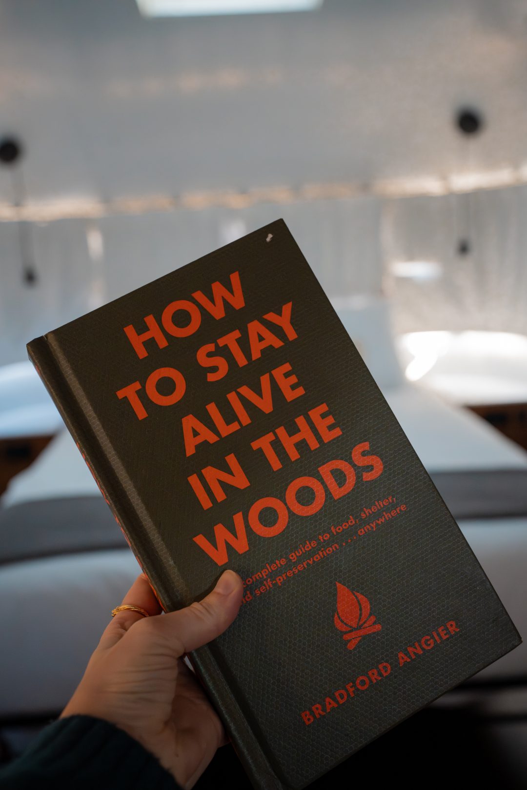 Travel Blogger Jordan Gassner holding up a "How To Stay Alive in the Woods" book at AutoCamp in Three Rivers, California