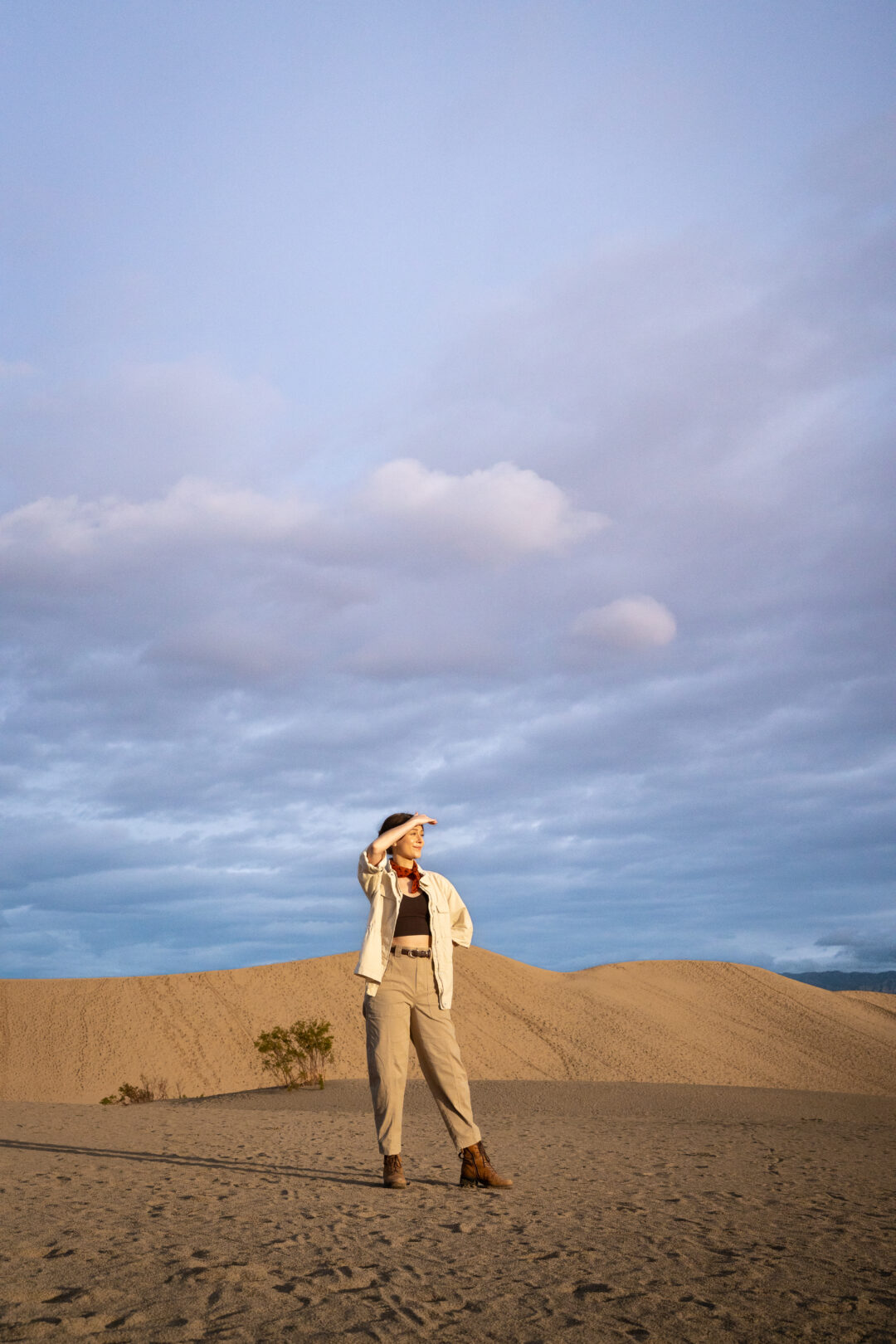Travel Blogger Jordan Gassner shielding her eyes from the sun while standing on the sand in Mesquite Flat Sand Dunes in Death Valley National Park