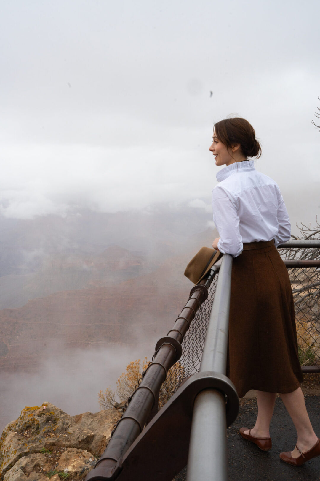 Travel Blogger Jordan Gassner smiling from a railing at Mather Point with mist and cloud partially obscuring the view of the Grand Canyon