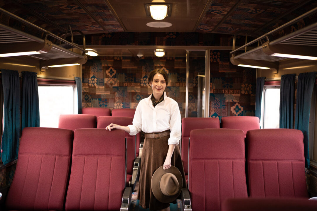 Travel Blogger Jordan Gassner smiling while standing in the aisle of a First Class car with pink seats inside the Grand Canyon Railway
