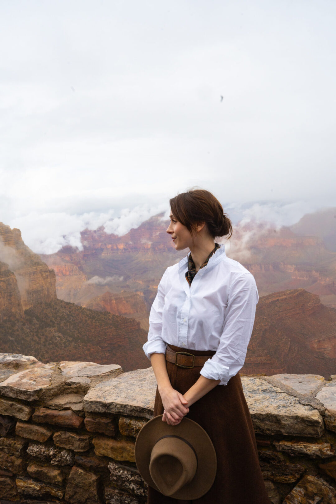 Travel Blogger Jordan Gassner standing and holding her hat while looking to her right along Rim Trail of the Grand Canyon near El Tovar