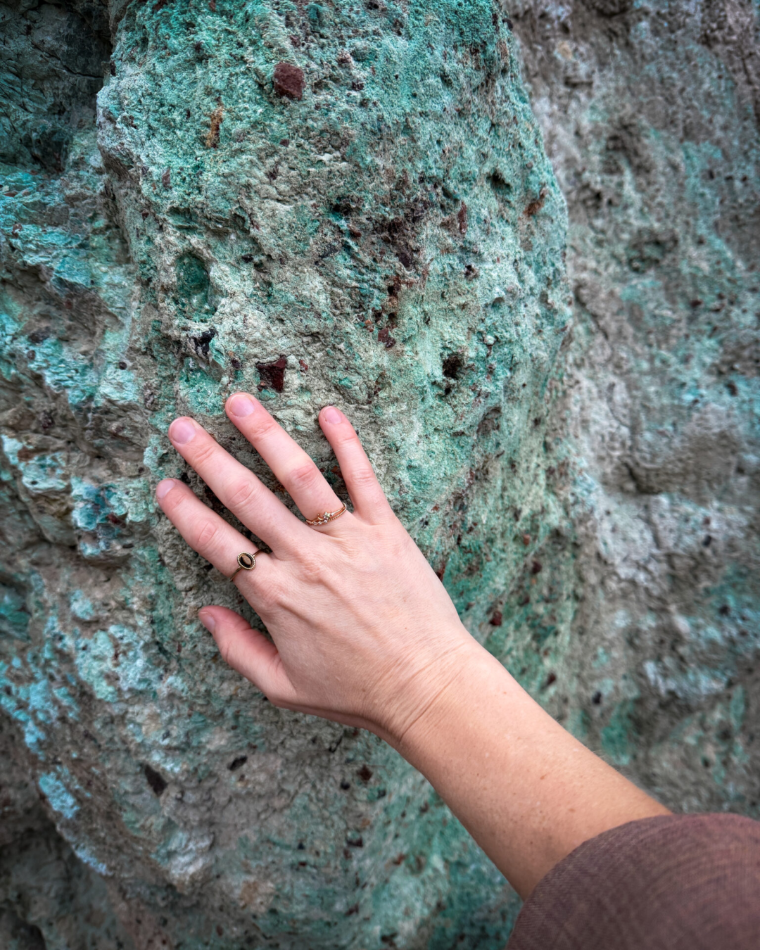 A woman's hand touching a naturally blue appearing rock inside Artist's Palette in Death Valley National Park, California, USA