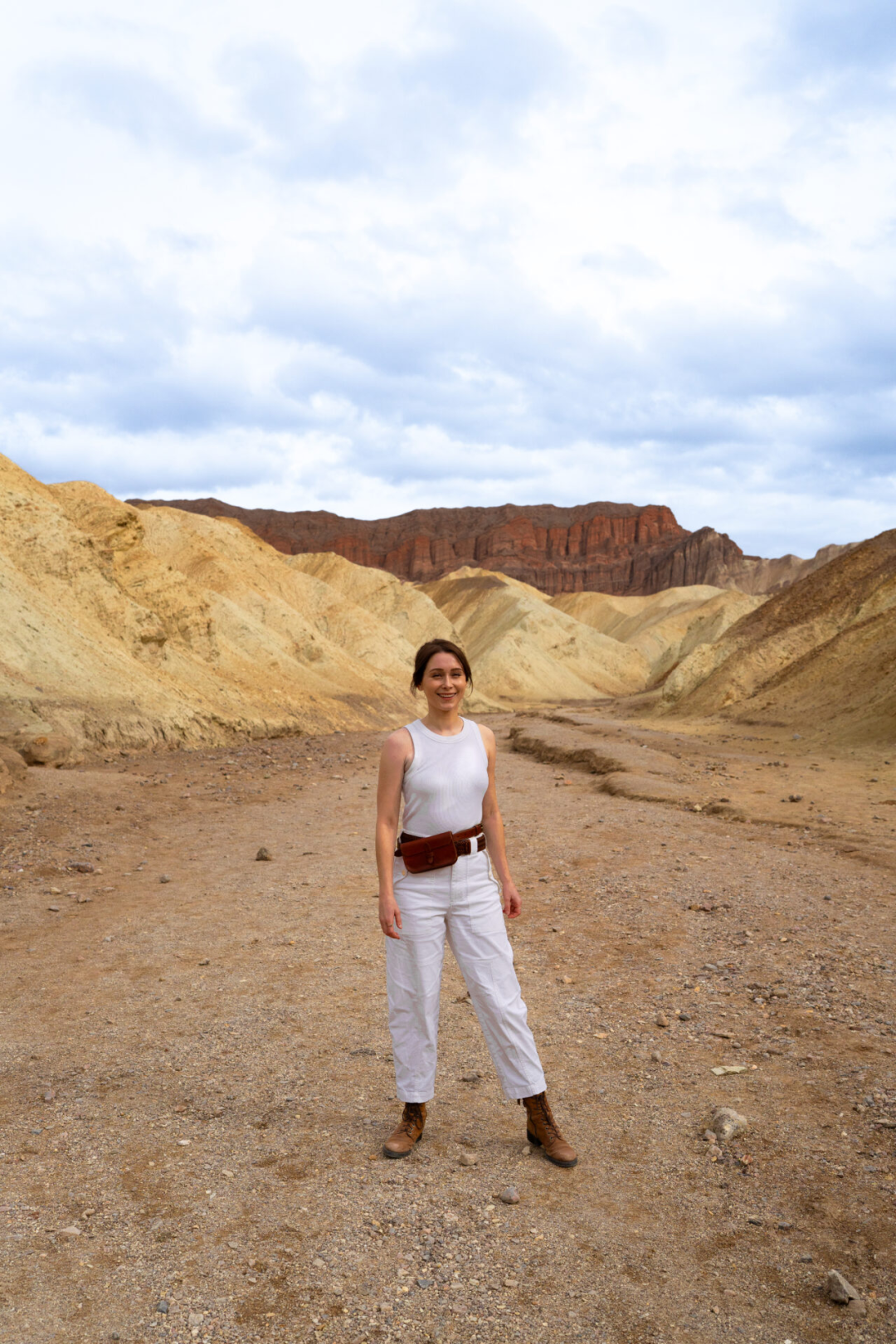 Travel Blogger Jordan Gassner smiling while walking along the Golden Canyon Trail with the Red Cathedral behind her behind inside in Death Valley National Park