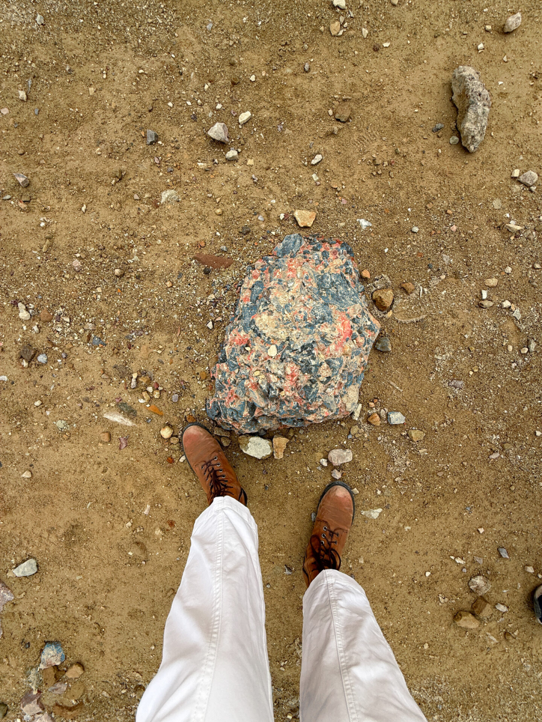 A woman in white pants and brown explorer boots standing next to a multicolored rock in Golden Canyon at Death Valley National Park
