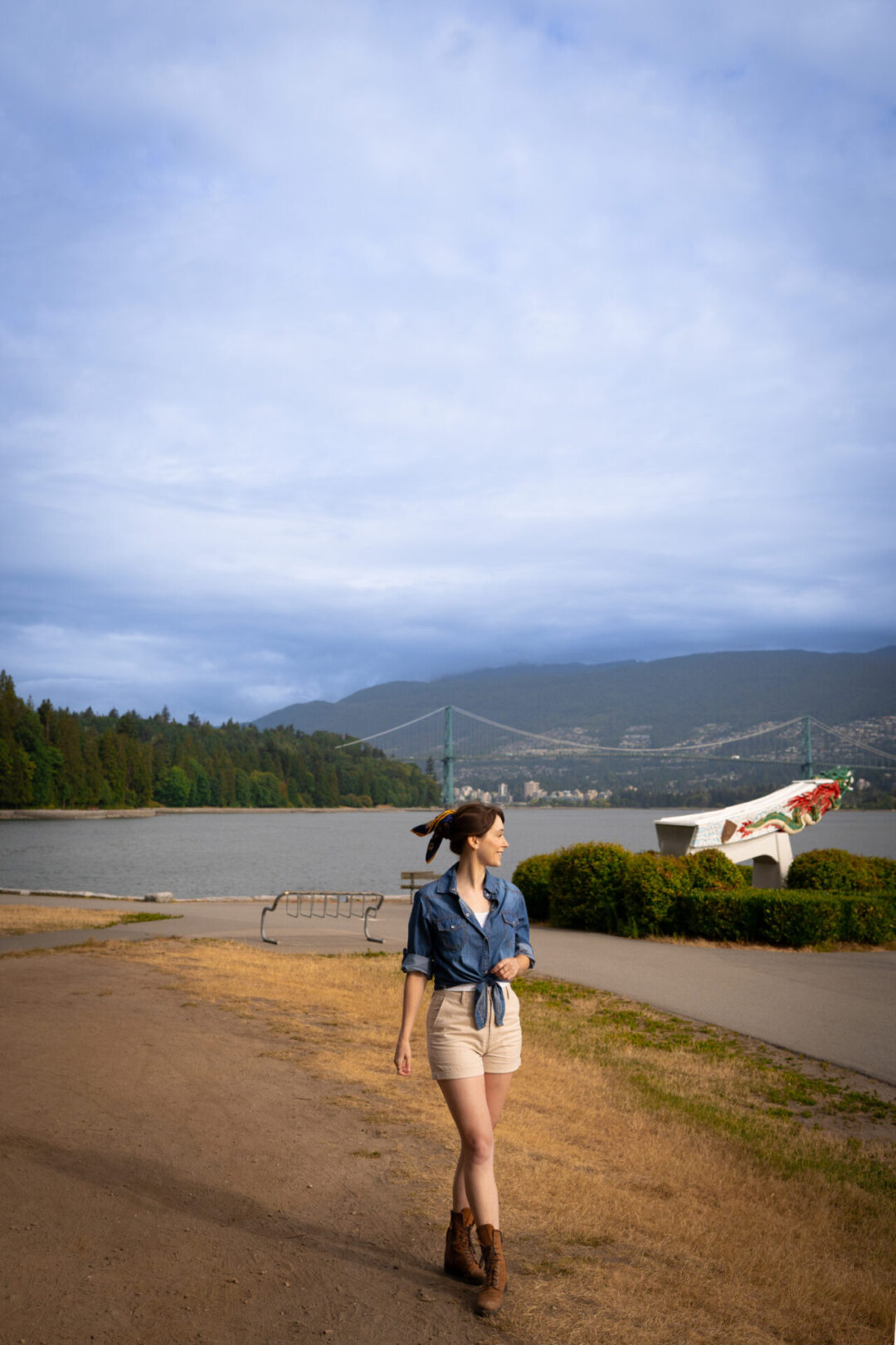 Travel Blogger Jordan Gassner standing and smiling in front of the S.S. Empress of Japan Figurehead Replica an a view of Lions Gate Bridge from Stanley Park in Vancouver, Canada