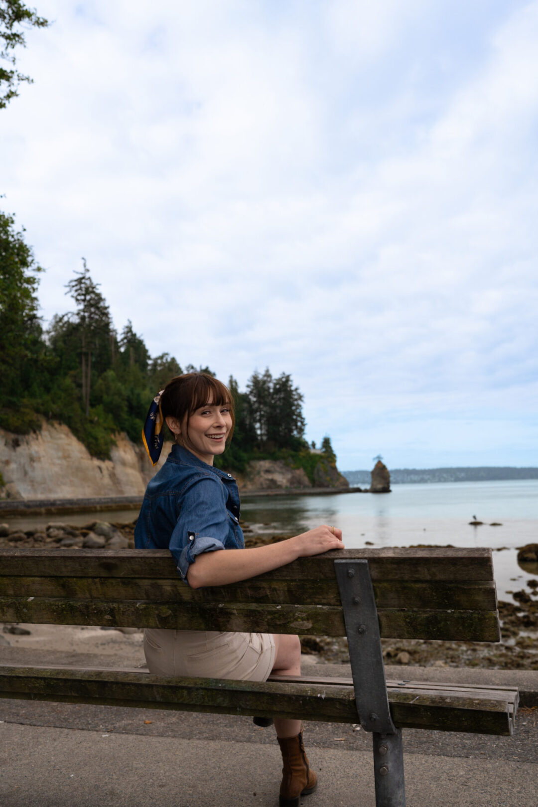 Travel Blogger Jordan Gassner turning around and smiling while sitting on a bench looking out toward Siwash Rock in Vancouver, Canada