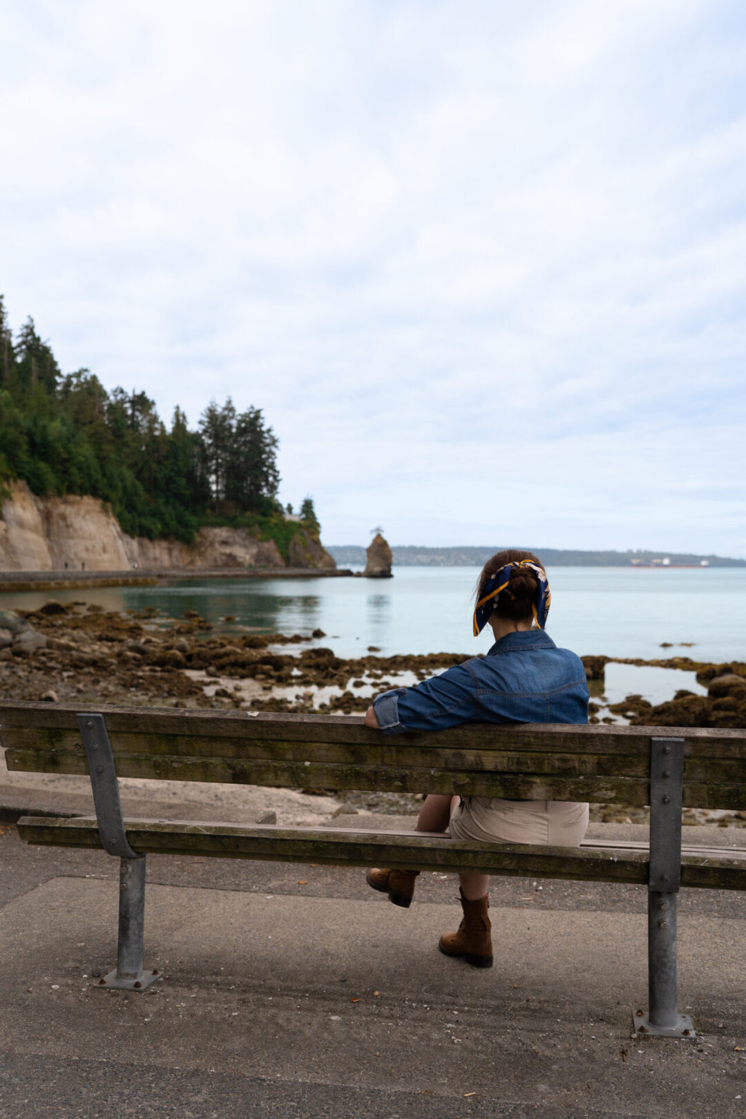 Travel Blogger Jordan Gassner leisurely sitting on a bench and looking toward Siwash Rock in Stanley Park