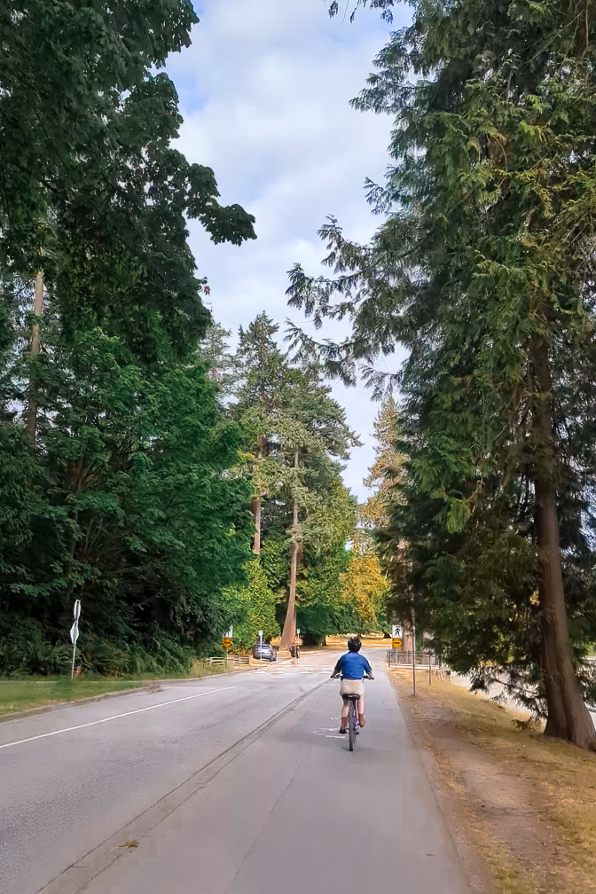 Travel Blogger Jordan Gassner cruising down a bike path next to a road inside Stanley Park in Vancouver, Canada