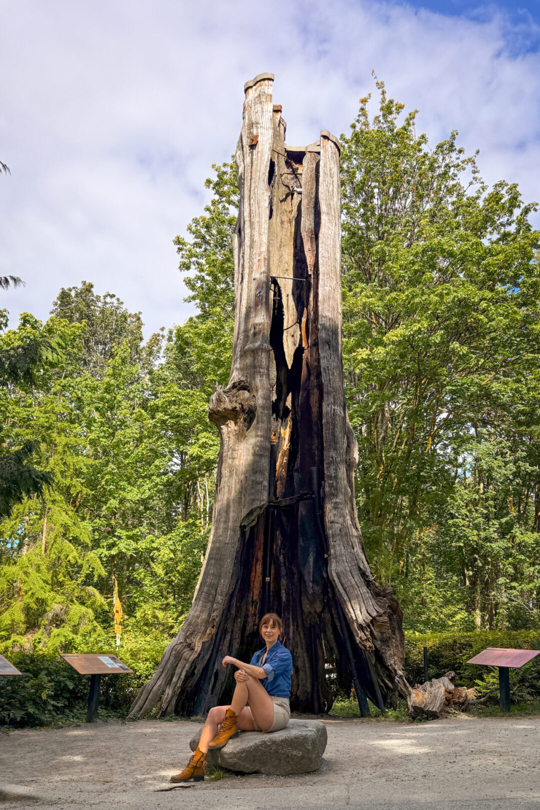 Travel Blogger sitting on a rock and smiling in front of Hollow Tree in Stanley Park in Vancouver, Canada