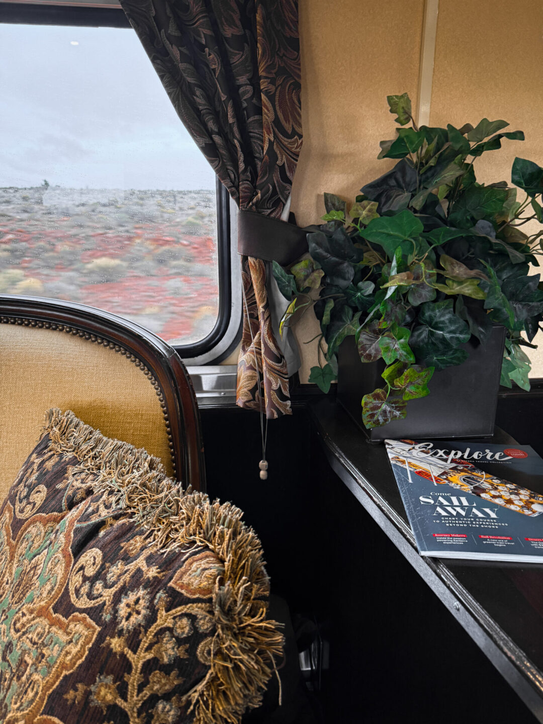 A close-up of a patterned pillow, matching curtains, faux plant, and magazine from a luxury parlor car inside the Grand Canyon Railway