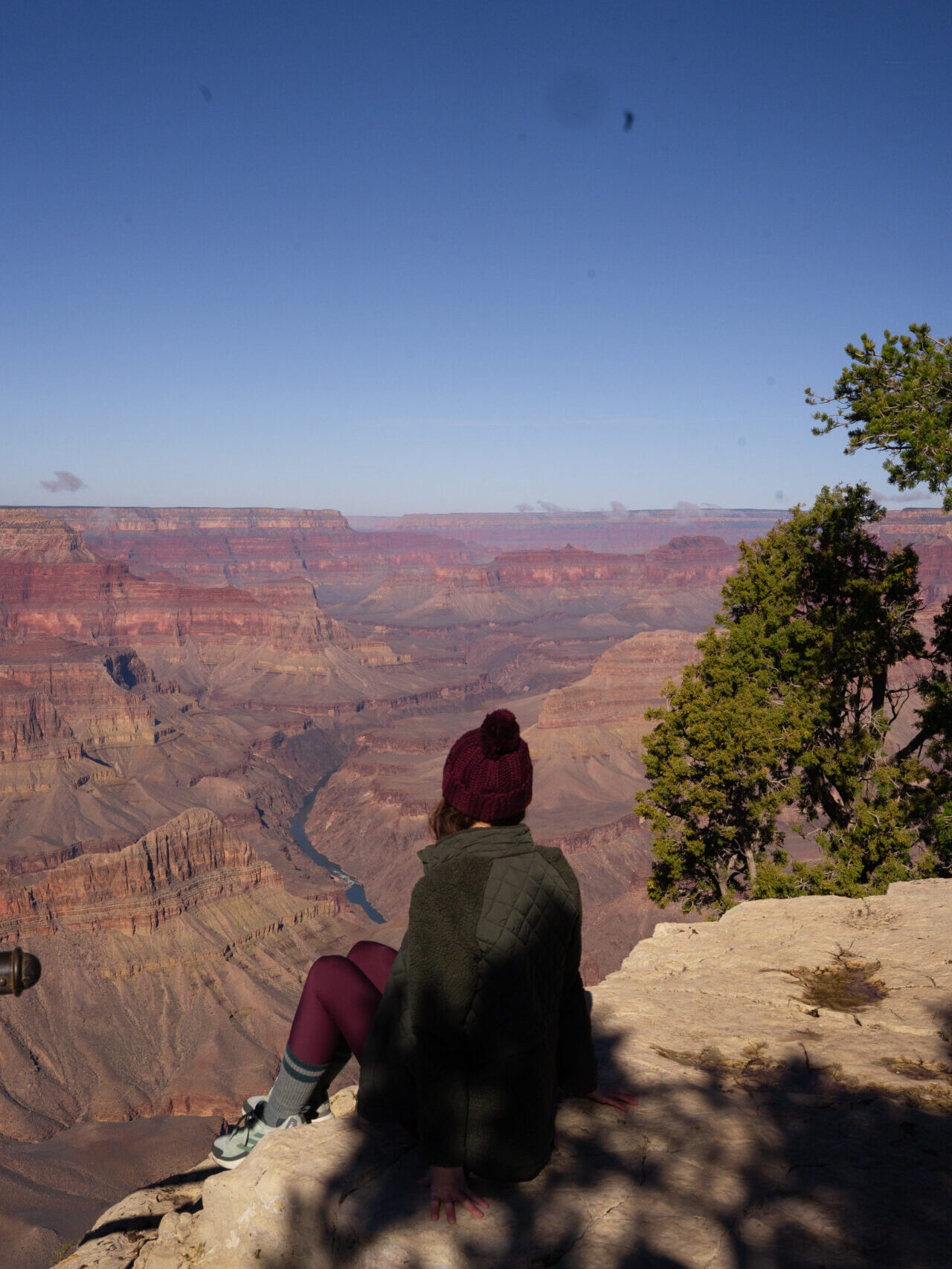 Travel Blogger Jordan Gassner wearing a winter jacket and sitting half in the sun, half in the shade at Mohave Point in the Grand Canyon