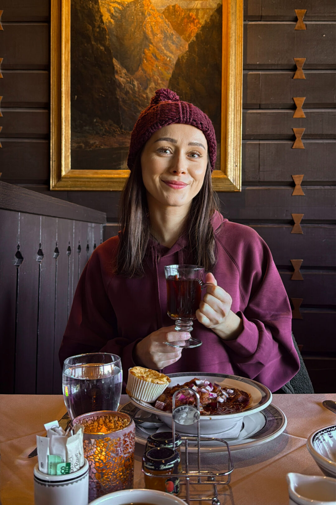Travel Blogger Jordan Gassner holding a hot apple cider and smiling with a bowl of chili in front of her at El Tovar in the Grand Canyon