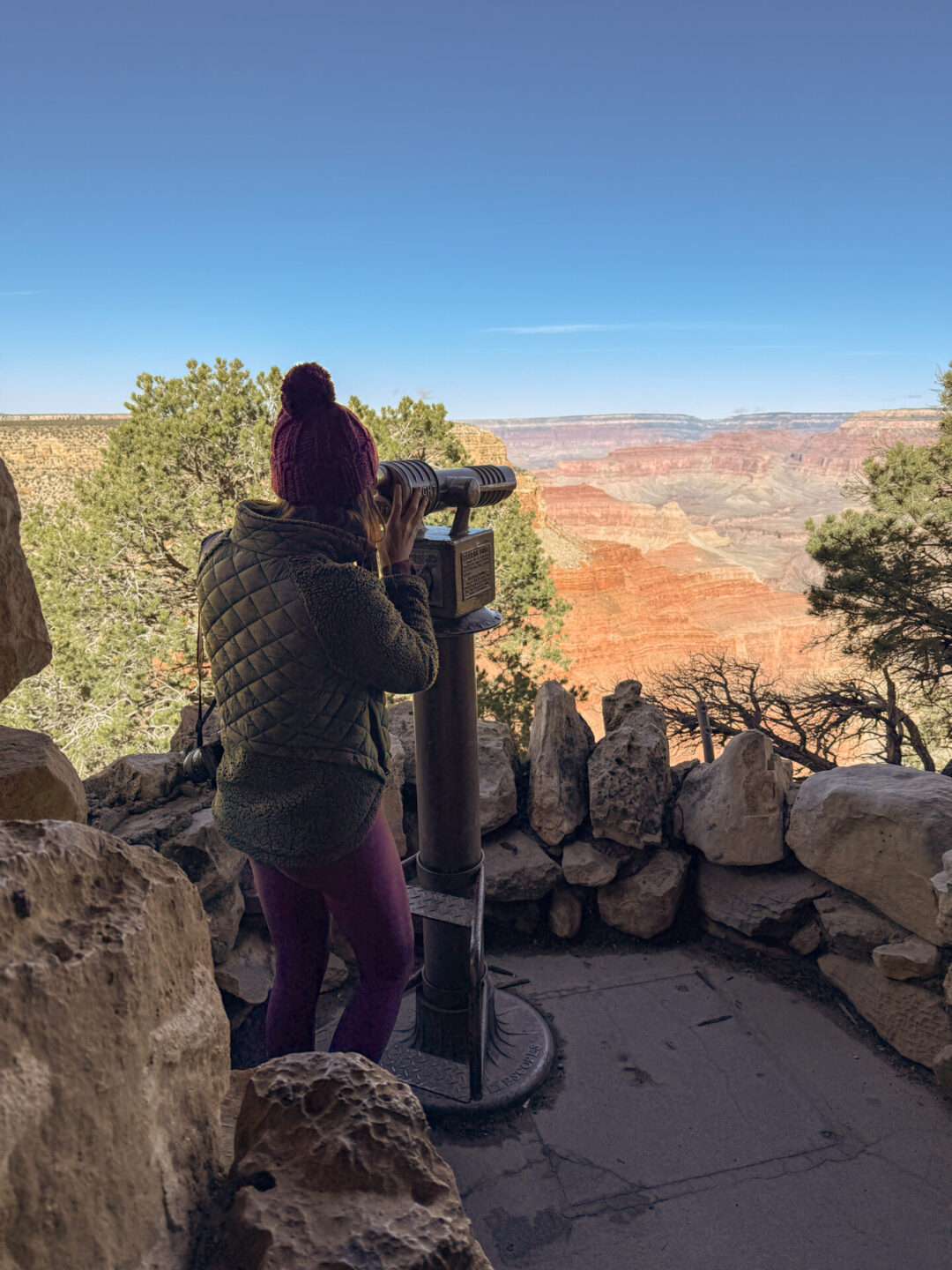Travel Blogger Jordan Gassner looking out through a built-in set of binoculars at Hermit's Rest in the Grand Canyon