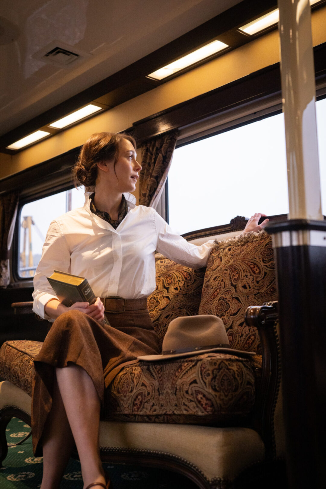 Travel Blogger Jordan Gassner sitting on a loveseat and looking over her shoulder and out the window of a Grand Canyon Railway luxury parlor car