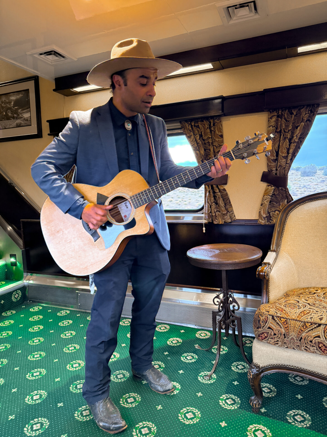 A musician singing and playing guitar while wearing a cowboy hat inside a Grand Canyon Railway car