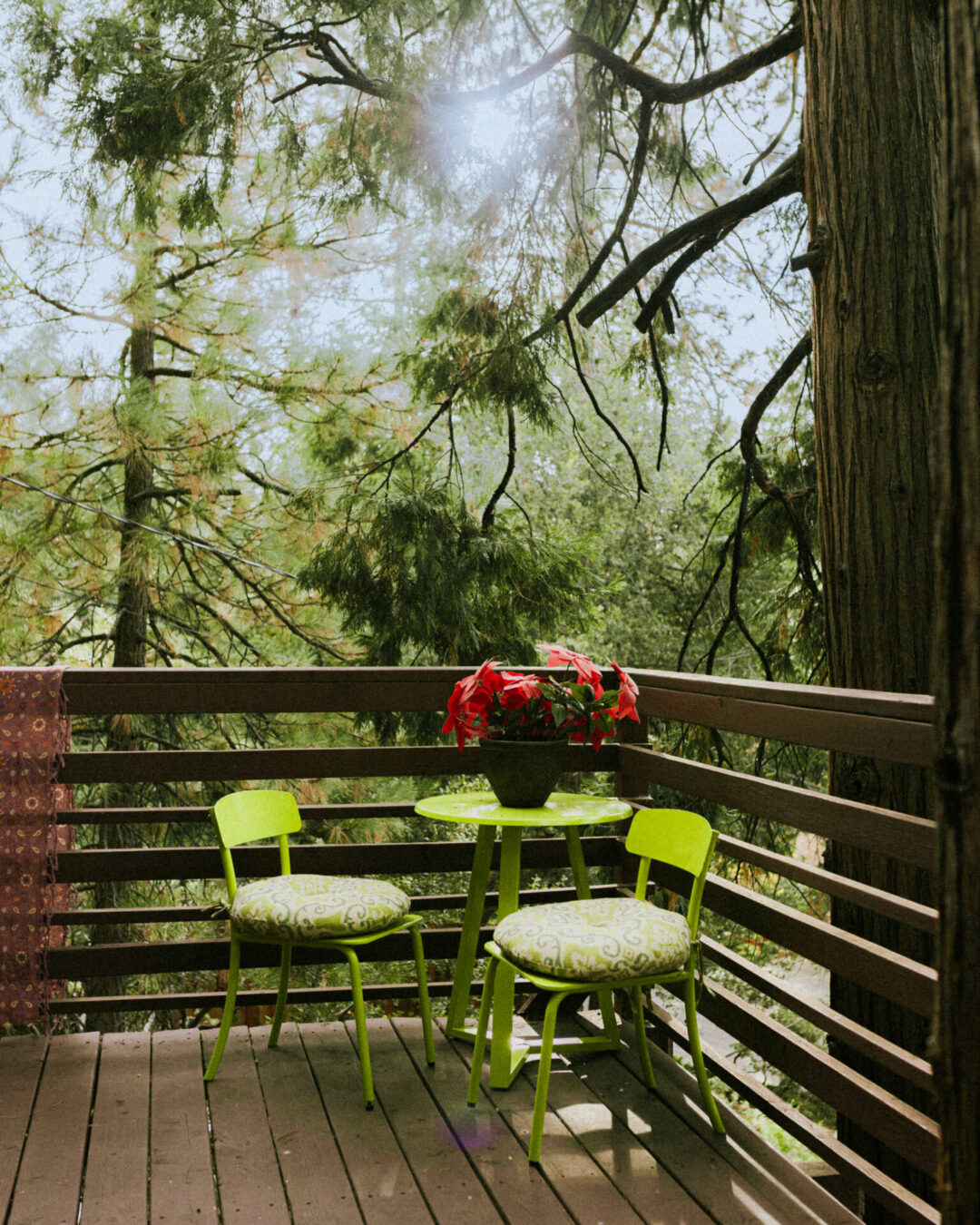 A deck with two bright green chairs and a matching bistro table with a pot of flowers sitting on the corner of a deck in Idyllwild, California, a great weekend trip from Los Angeles