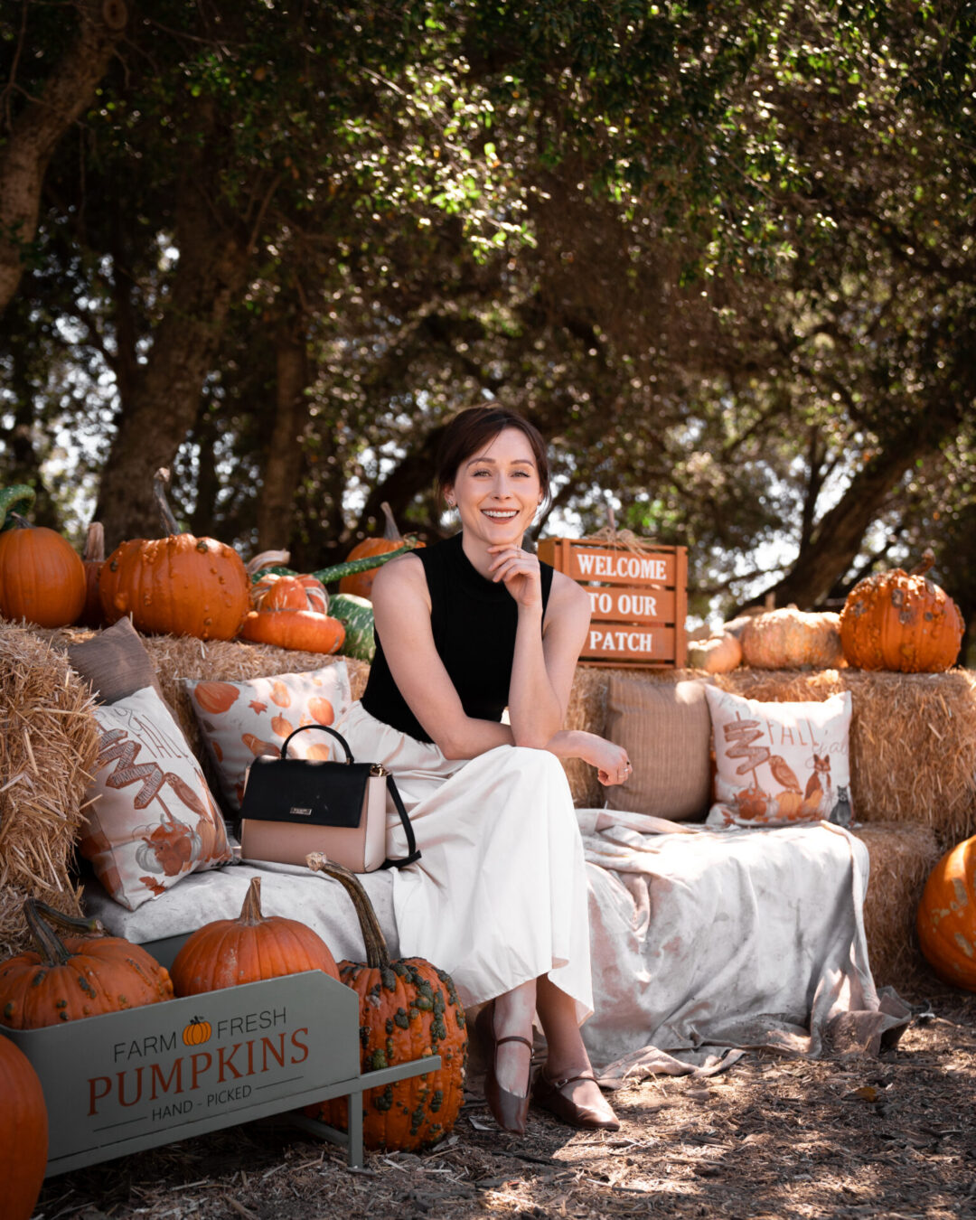 Travel Blogger Jordan Gassner sitting on a few hay bales near a group of pumpkins in Julian, California