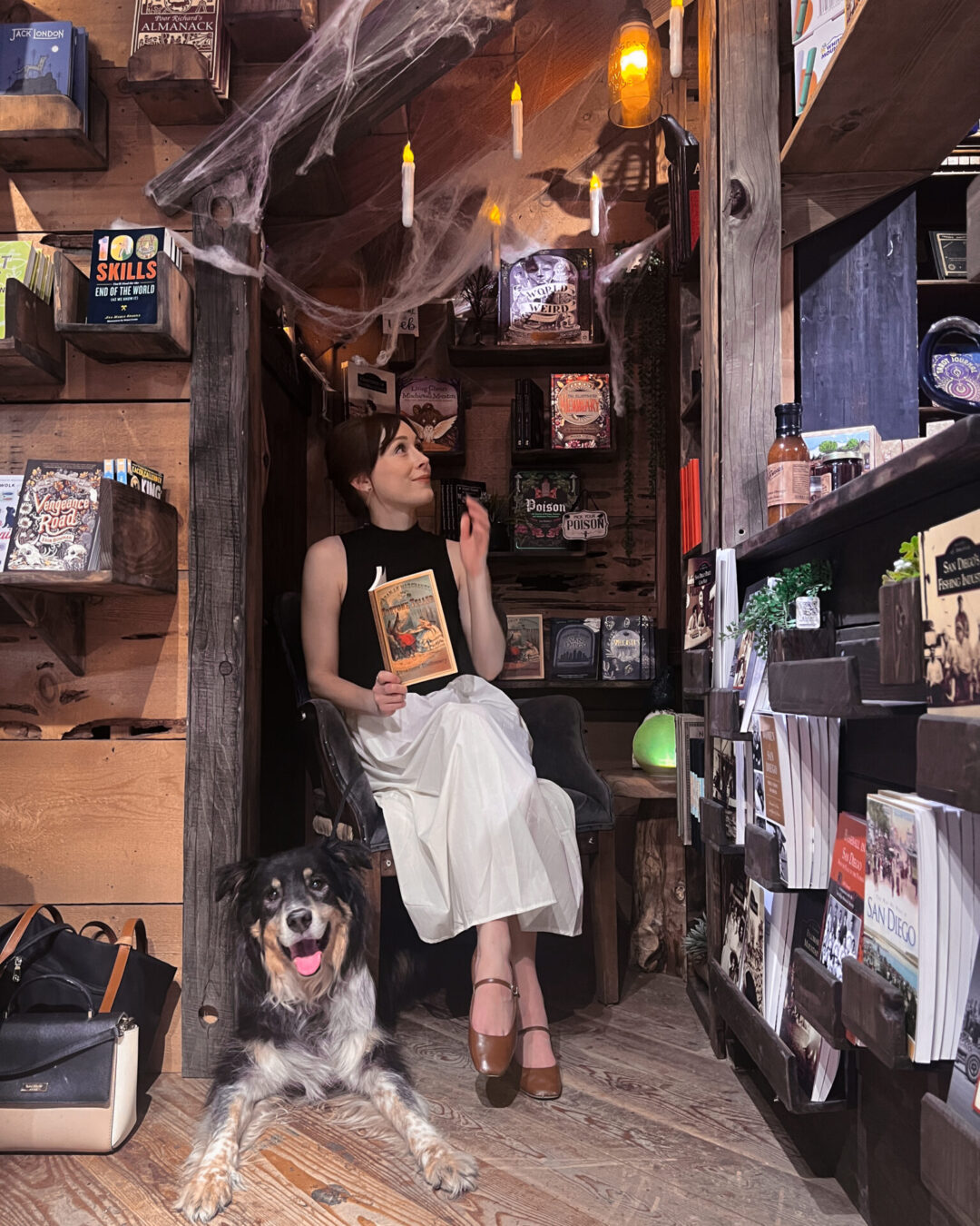 Travel Blogger Jordan Gassner holding a book while sitting in a chair next to a dog inside the Warm Hearth  amid Halloween decorations in Julian, California