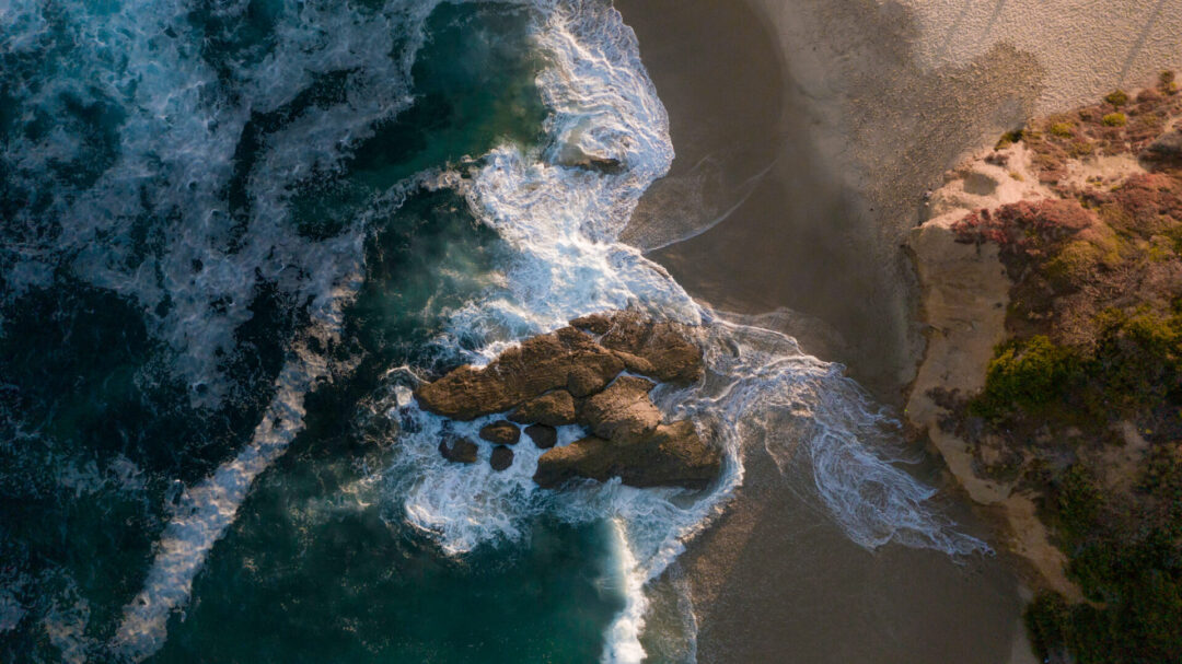 An aerial shot of waves crashing against rocks in Laguna Beach, California