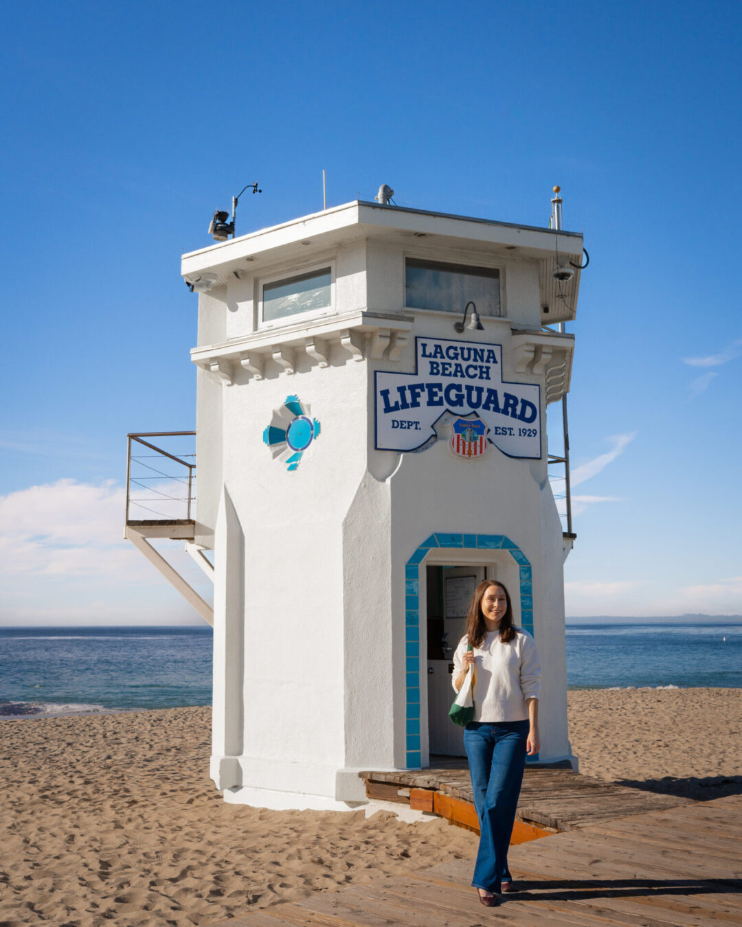 Travel Blogger Jordan Gassner smiling in front of the old lifeguard tower at Main Beach in Laguna Beach, California