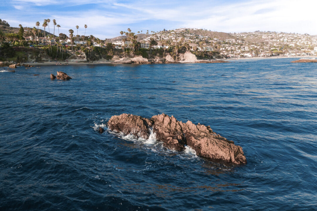 A rock in the middle of the ocean with the Laguna Beach coastline in the background