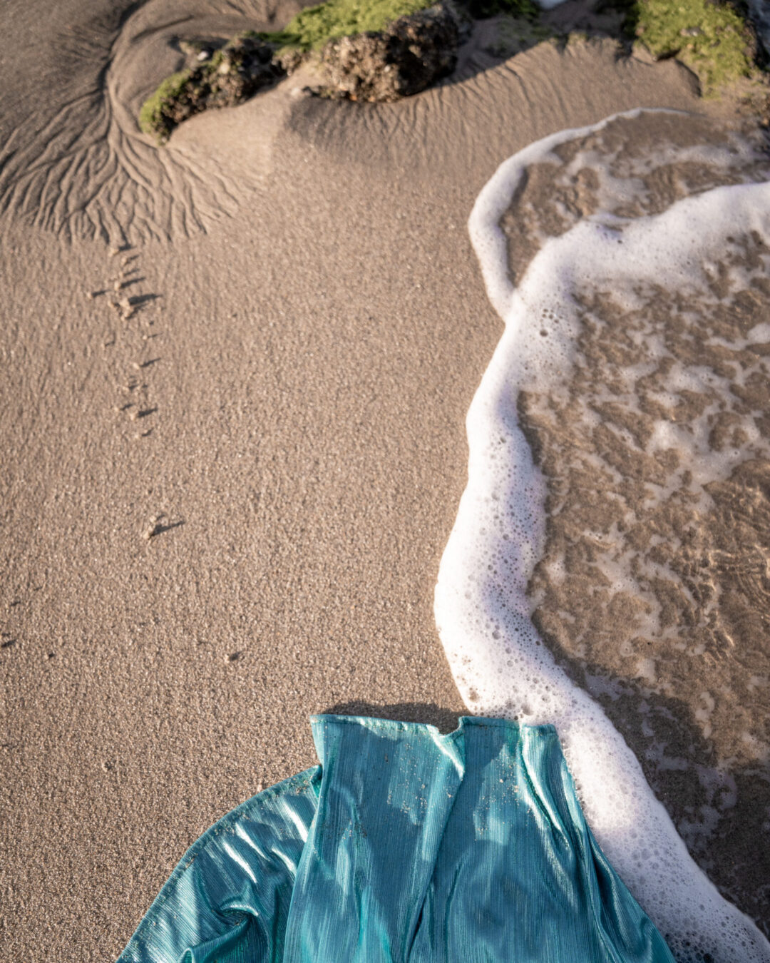 The hem of a blue mermaid dress touching the sand and waves along Victoria Beach in Laguna Beach
