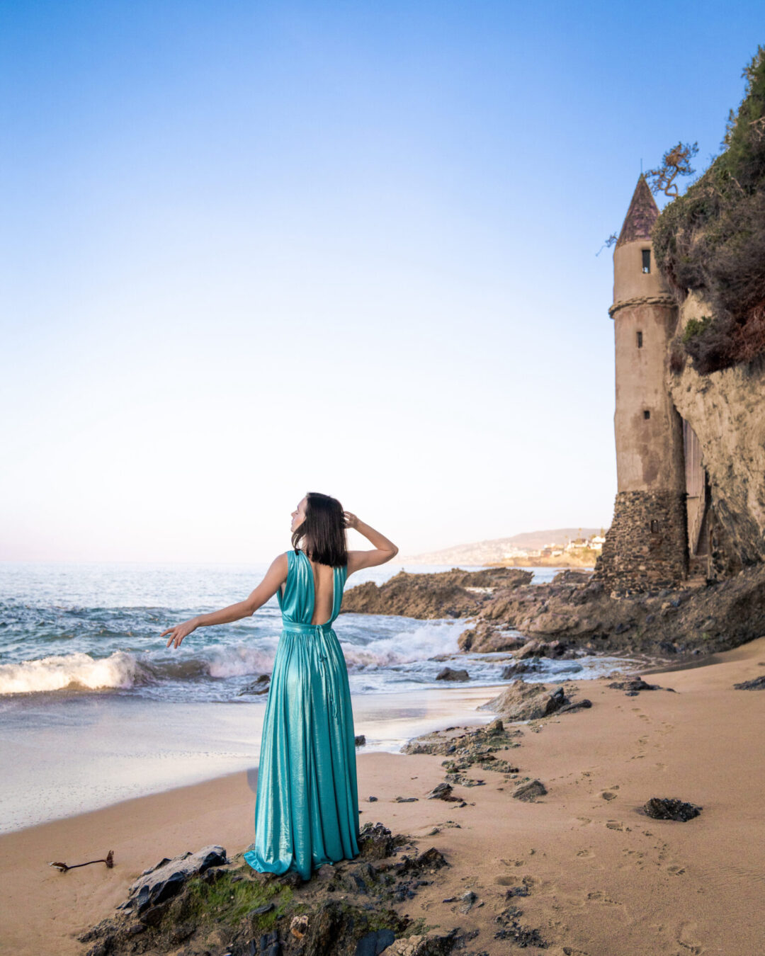 Travel Blogger Jordan Gassner wearing a blue mermaid dress and standing on Victoria Beach near Pirate Tower in Laguna Beach