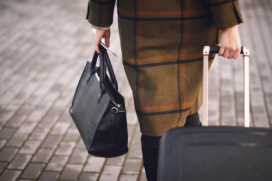 A woman holding a purse, boarding pass, and rolling a suitcase
