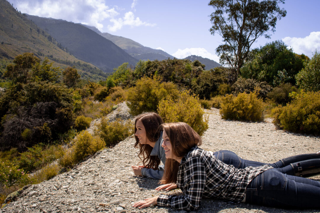 Travel Blogger Jordan Gassner and her friend crouching down at a spot outside Queenstown, New Zealand just like Frodo and Sam do when they spot the oliphant in the Lord of the Rings films
