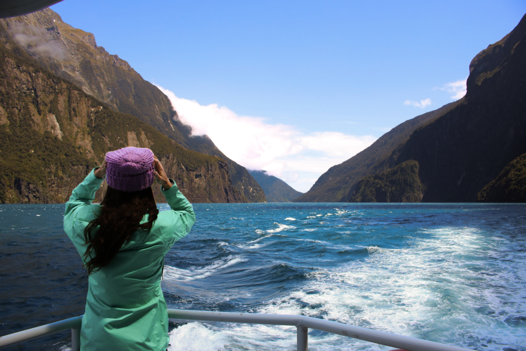 Travel Blogger Jordan Gassner holding onto her beanie while on a Milford Sound Cruise, about an hour away from Queenstown, New Zealand