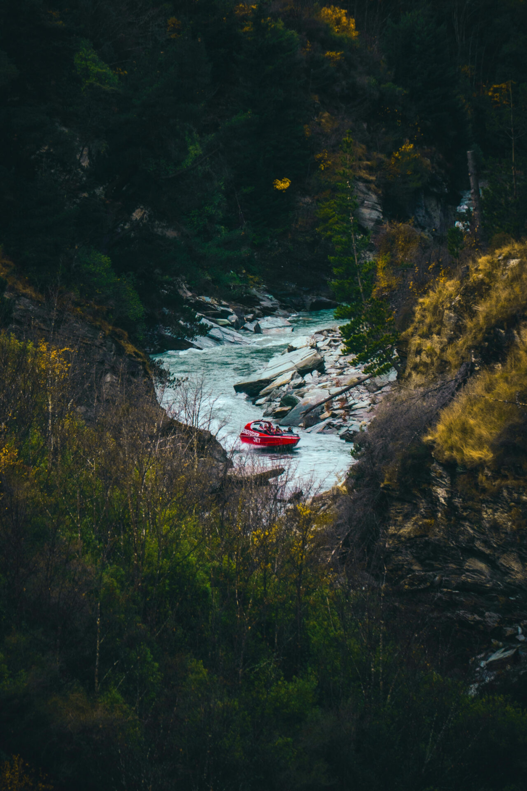 A red jet boat going gliding through the narrow slot canyons of the Shotover River in Queenstown, New Zealand