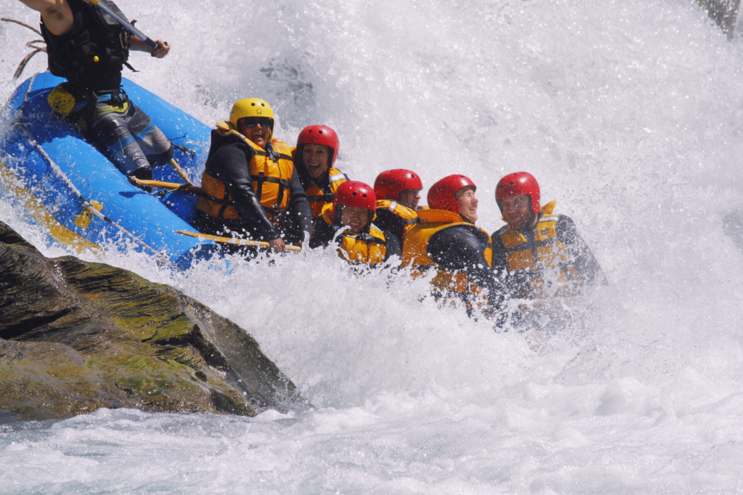Travel Blogger Jordan Gassner and a friend smiling while going over a grade 5 white water rapid on the Shotover River in Queenstown, New Zealand